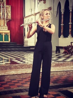 A woman in a black jumpsuit playing the flute in a cathedral